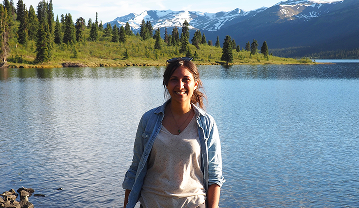 Woman standing by body of water with green landscape and mountains in the background