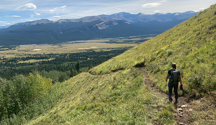 Person walking down trail with a mountain valley in the background