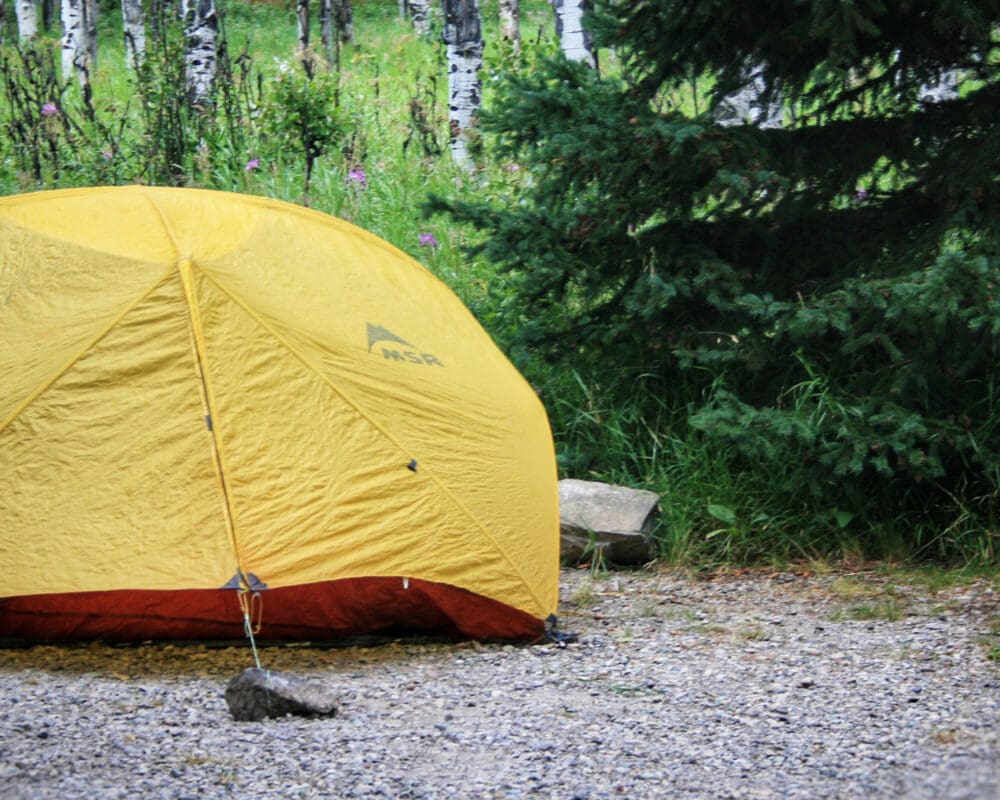 A yellow tent on a camping pad in the forest
