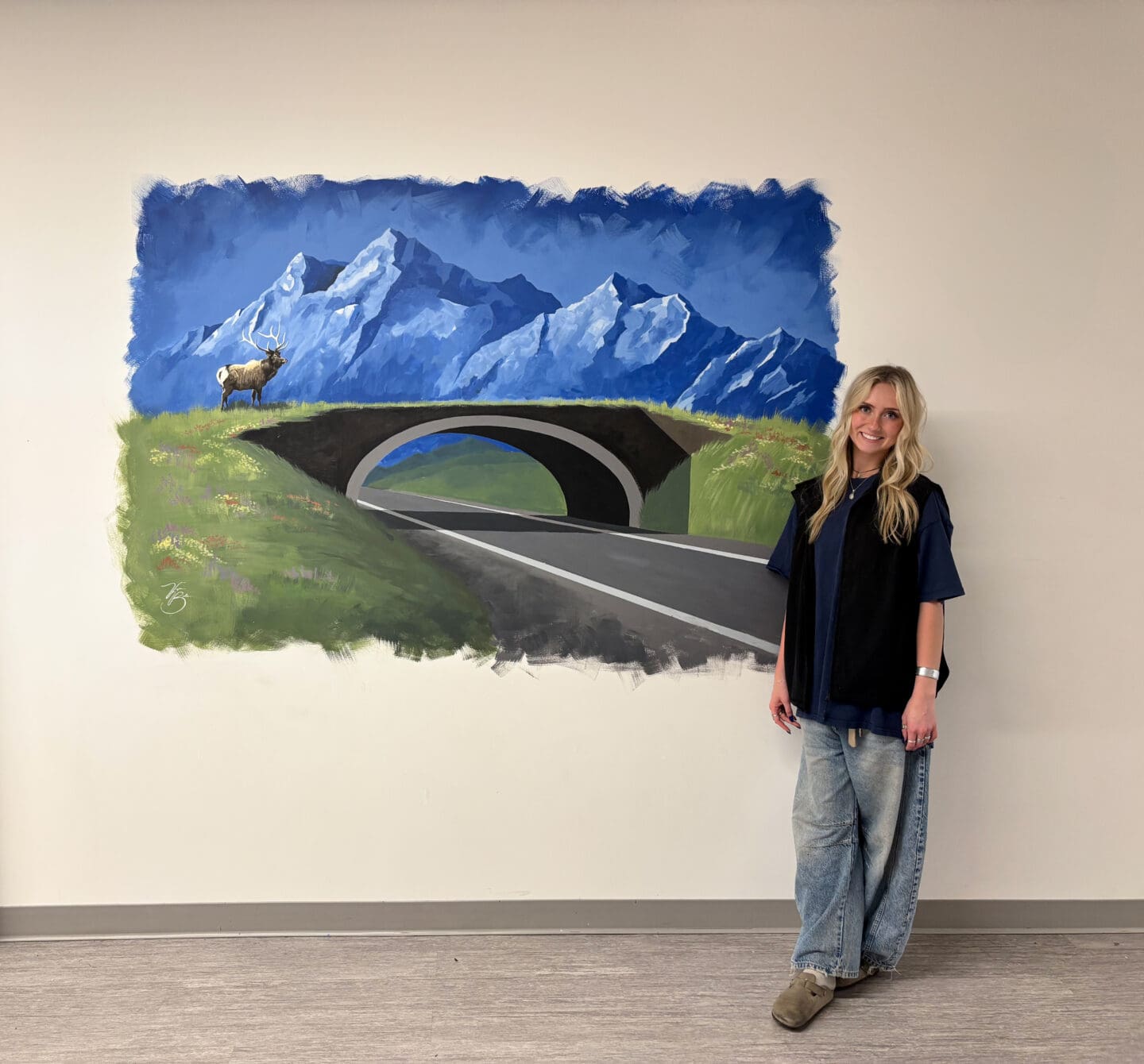 A student stands in front of her mural of a wildlife crossing in a Bozeman, Montana high school.
