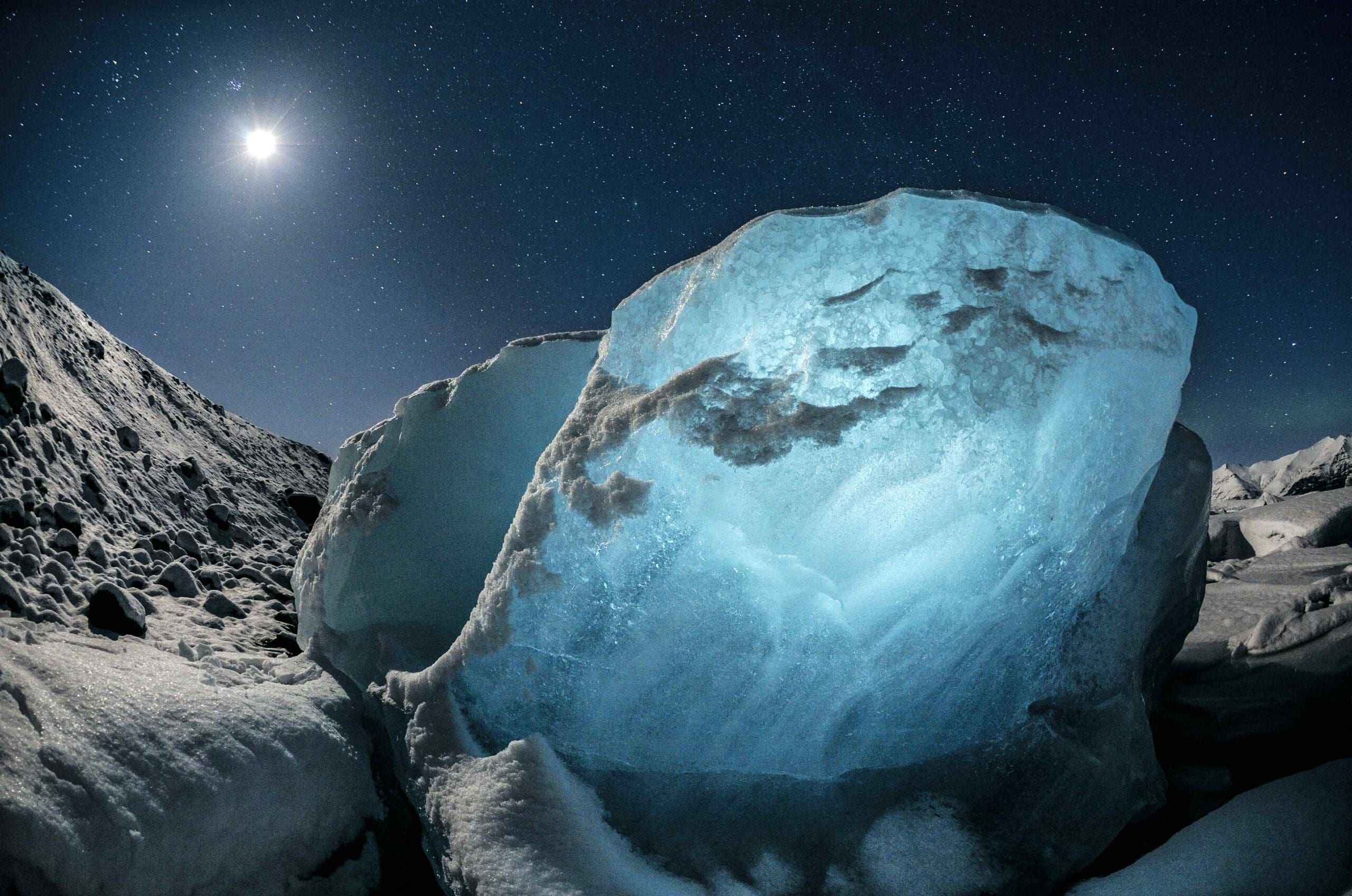 A blue chunk of ice on a beach at night